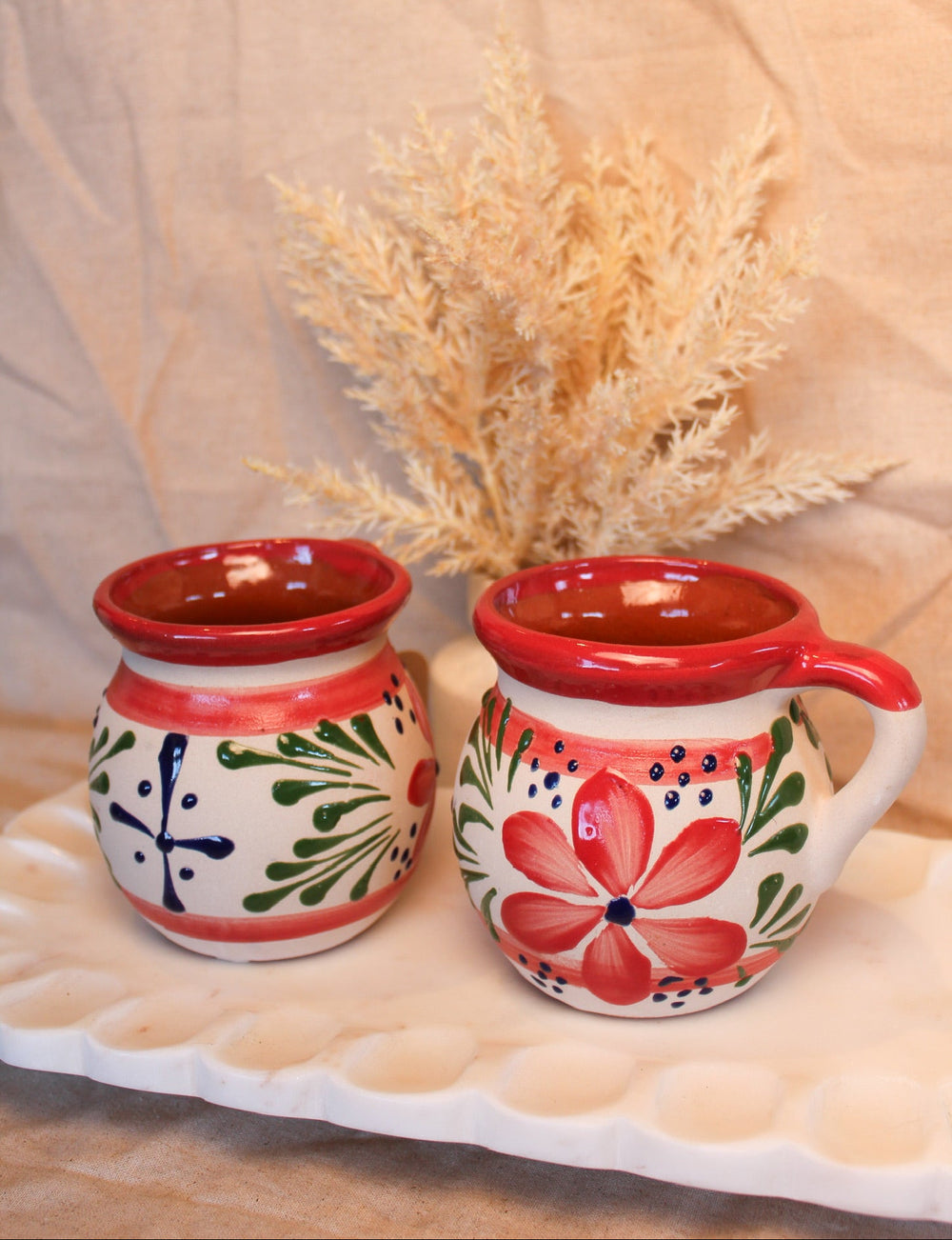 Two ceramic mugs with floral designs on a beige surface with a light background
