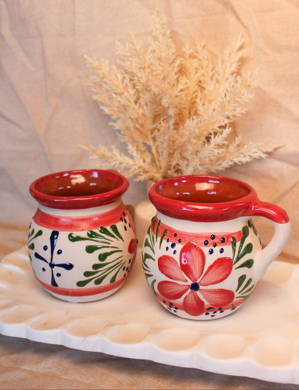 Two ceramic mugs with floral designs on a beige surface with a light background